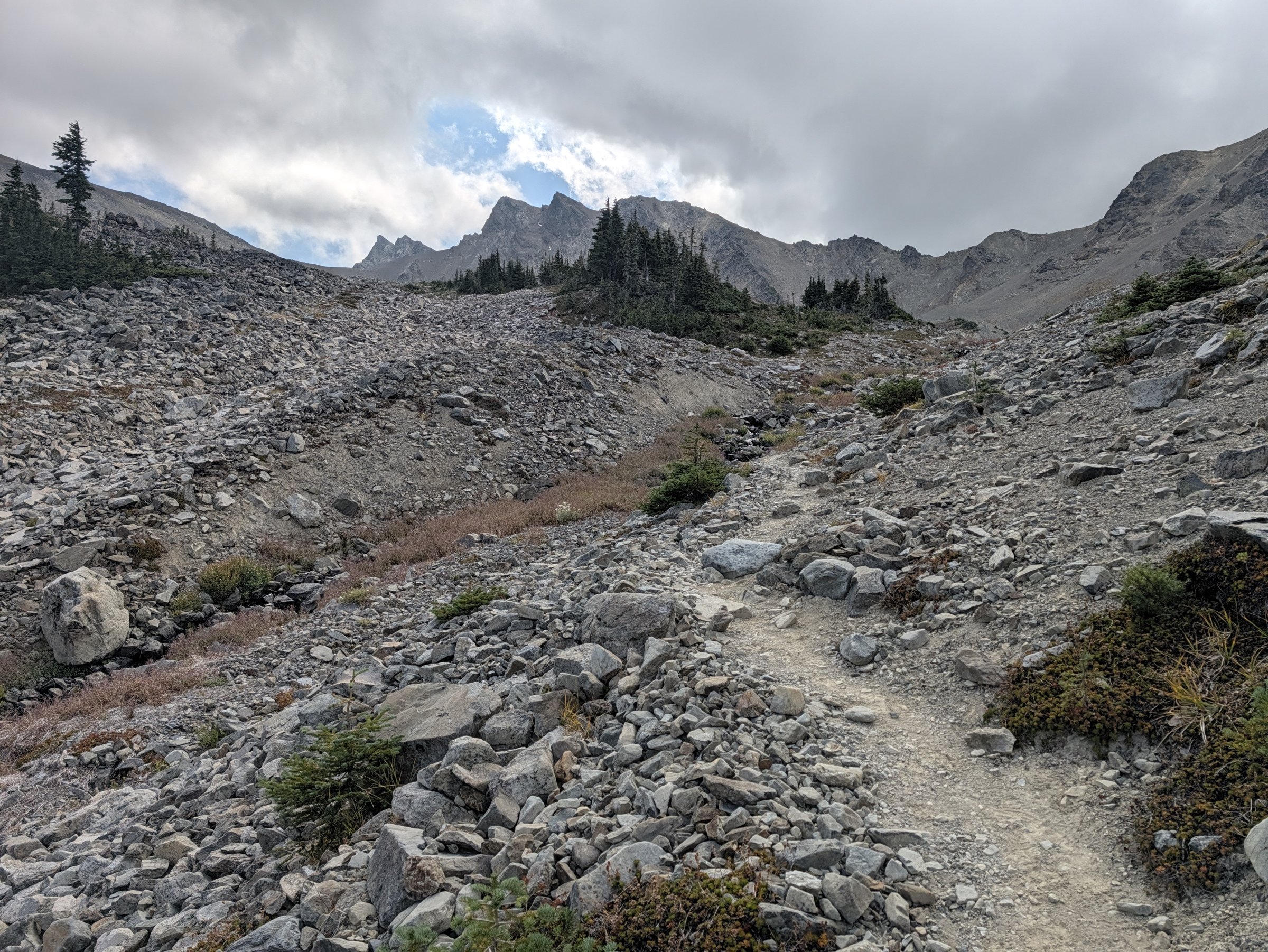 A rocky talus trail climbing toward jagged peaks under heavy clouds